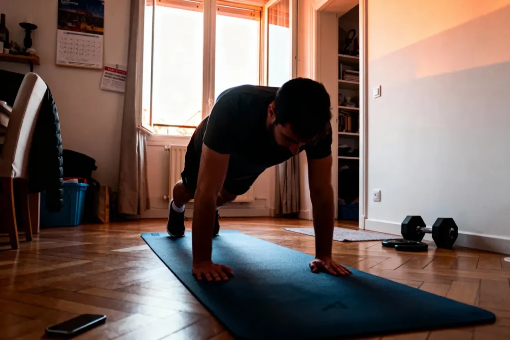 Homme faisant des pompes sur tapis dans un salon, halteres à proximité, lumière naturelle.